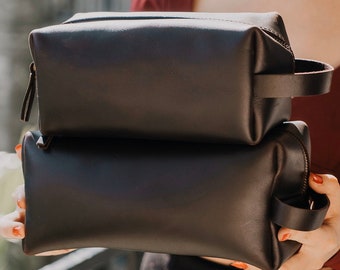 May include: Two brown leather zippered travel bags stacked on top of each other.