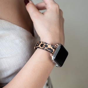 May include: A silver and black smartwatch with a leopard print leather band. The band has rose gold accents.