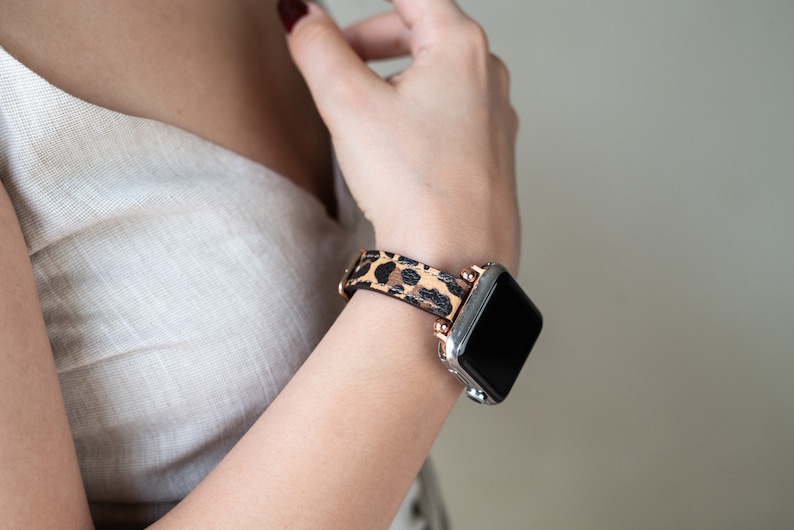 May include: A silver and black smartwatch with a leopard print leather band. The band has rose gold accents.