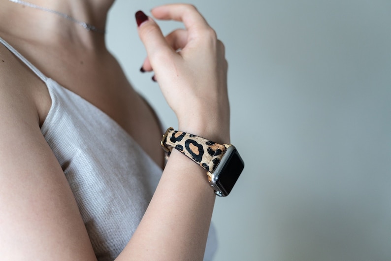 May include: A close-up of a person's wrist wearing a smartwatch with a leopard print band. The watch face is black and the band is brown and black.