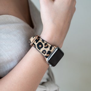 May include: A black smartwatch with a leopard print band. The band is made of brown and black faux fur.