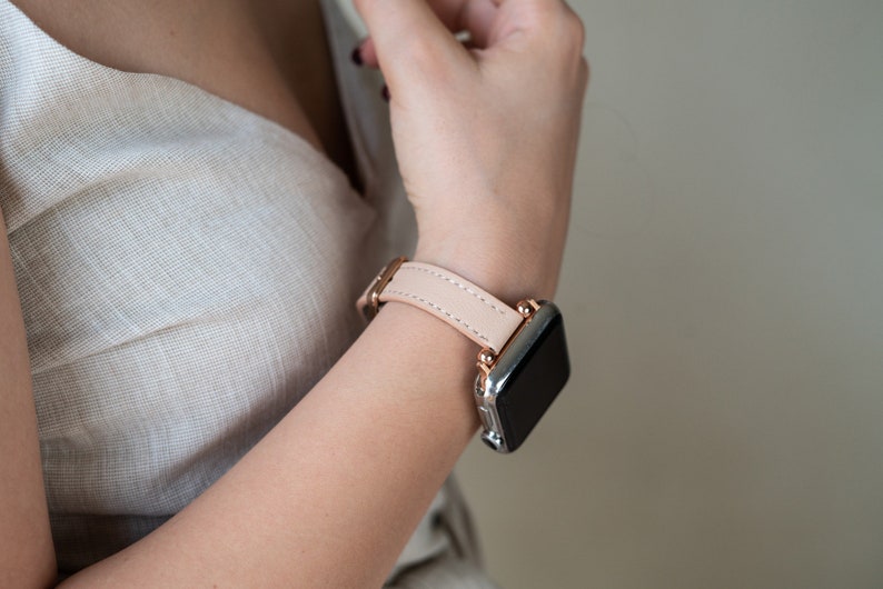 May include: A light pink leather watch band with a rose gold buckle and a silver smartwatch.