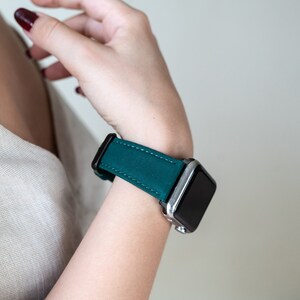 May include: A teal green leather watch band with a silver and black smartwatch.