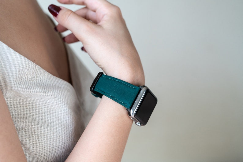 May include: A teal green leather watch band with a silver and black smartwatch.