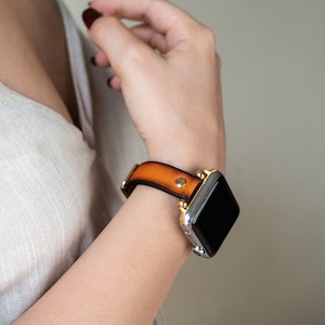 Op de afbeelding: Een bruin leren horlogebandje met gouden accenten en een zwart smartwatch-scherm.
