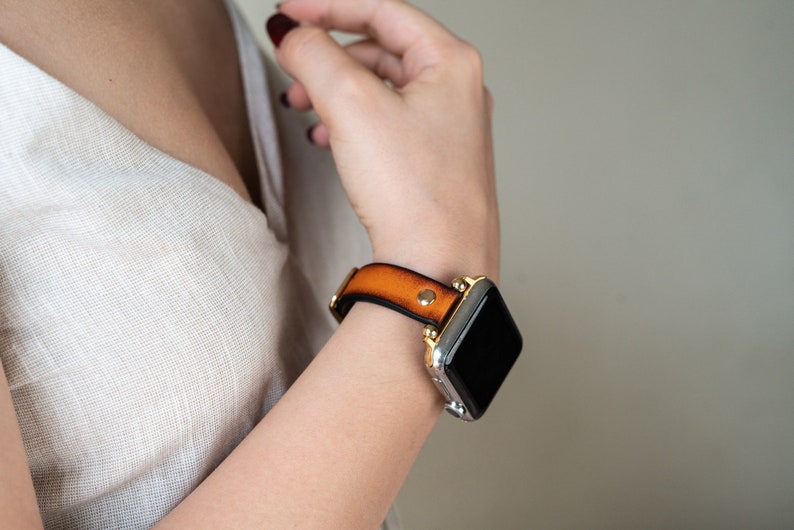Op de afbeelding: Een bruin leren horlogebandje met gouden accenten en een zwart smartwatch-scherm.