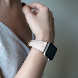 May include: A close-up of a person's wrist wearing a silver and black Apple Watch with a light pink leather band.