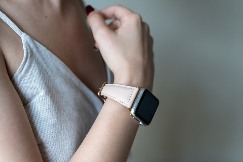 May include: A close-up of a person's wrist wearing a silver and black Apple Watch with a light pink leather band.