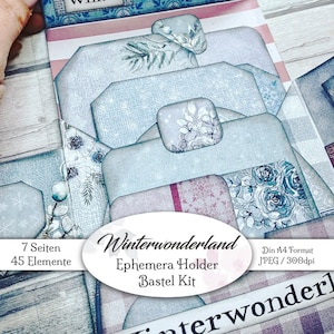 Könnte beinhalten: Ein blauer und weiß gemusterter Papierephemera-Halter mit dem Text "Winterwonderland Ephemera Holder Bastel Kit" und "7 Seiten 45 Elemente". Der Halter ist dazu gedacht, Papierephemera für Scrapbooking oder Kartenherstellung aufzubewahren.