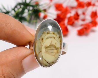 Könnte beinhalten: Ovale Silberring mit einem polierten Stein, der ein einzigartiges Muster aus beige- und graufarbenen Wirbeln aufweist. Der Ring hat eine schlichte, polierte Silberfassung, die die natürliche Schönheit des Steins hervorhebt. Ein auffälliges Schmuckstück.