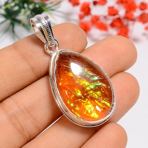 May include: A teardrop-shaped pendant with a vibrant, iridescent gemstone. The gem displays fiery orange, yellow, and green hues, set in a silver metal frame. The pendant has a silver bail for attaching to a chain.
