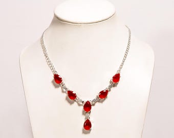 May include: A silver necklace with a series of teardrop-shaped, bright red gemstones. The gemstones are set in a silver metal frame and are connected by a delicate chain. The necklace is displayed on a white mannequin bust.