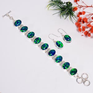 Può includere: Un set di bracciale e orecchini in argento. I gioielli presentano pietre preziose ovali blu e verdi incastonate in argento. Il bracciale ha una chiusura a toggle e gli orecchini hanno chiusure a gancio. Il set è esposto su una superficie bianca.