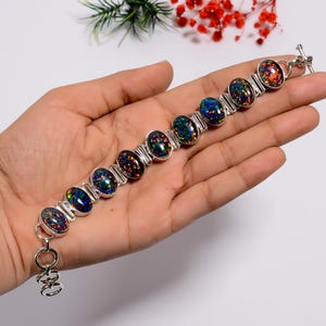 以下が含まれることがあります： 楕円形の黒オパールが特徴のシルバーブレスレット。ブレスレットは、オパールを繋ぐ個々のリンクで構成されており、留め金が付いています。オパールは、青、緑、赤など、さまざまな色を表示しています。