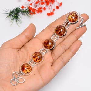 May include: A silver bracelet featuring five large, round amber stones. The amber stones have a warm, honey-like color with visible inclusions. The bracelet is connected by silver links and has a toggle clasp. The bracelet is displayed on a hand.