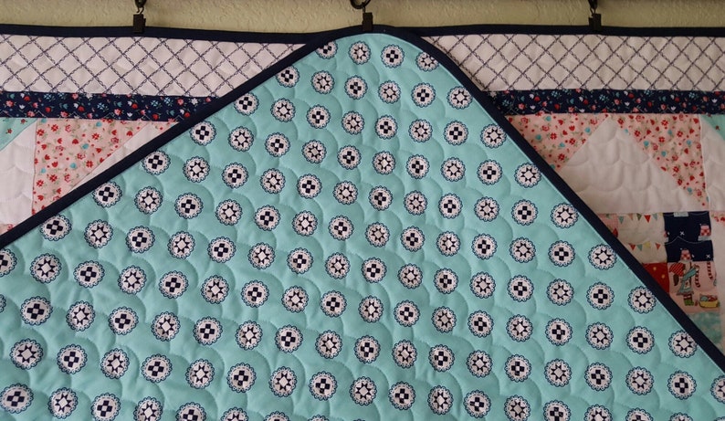 Op de afbeelding: Een turquoise blauwe quilt met een wit en zwart patroon. De quilt is gestikt met een cirkelvormig patroon. De quilt heeft een donkerblauwe bies.