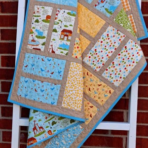 May include: A patchwork quilt featuring various fabric squares with prints of zoo animals, colorful balloons, birds, and floral patterns. The squares are separated by tan fabric sashing and finished with a bright blue polka dot fabric border.