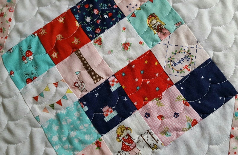 Op de afbeelding: Een patchworkdeken met een verscheidenheid aan kleurrijke stoffen, waaronder rood, blauw, roze en wit. De deken is gemaakt van vierkanten met verschillende patronen, waaronder bloemen, sterren en geometrische vormen. De deken is gestikt met een golvend steekpatroon.