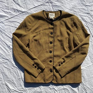 May include: A yellow and black checkered blazer with black buttons and a black trim around the collar, cuffs, and hem. The label reads "Ruth Stevens".