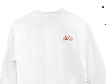 Op de afbeelding: Witte longsleeve trui met een klein geborduurd beeld van een oranje fiets op de linker borst.
