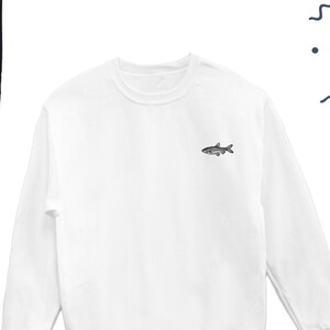 K&ouml;nnte beinhalten: Wei&szlig;er Langarm-Pullover mit einem kleinen gestickten Fischmotiv auf der Vorderseite.