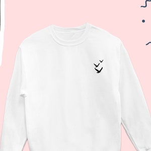 May include: White long-sleeved sweatshirt with a small black bird design on the left chest.