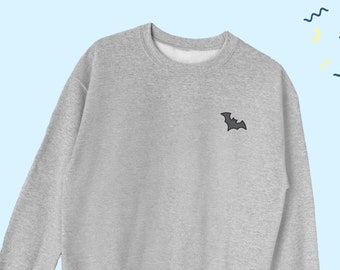 May include: A gray sweatshirt with a small black bat embroidered on the left chest. The sweatshirt is a classic crew neck style with long sleeves and a relaxed fit.