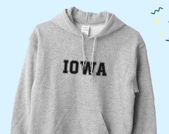 May include: A gray hooded sweatshirt with the word "IOWA" printed in black on the front. The sweatshirt has a kangaroo pocket and a drawstring hood.