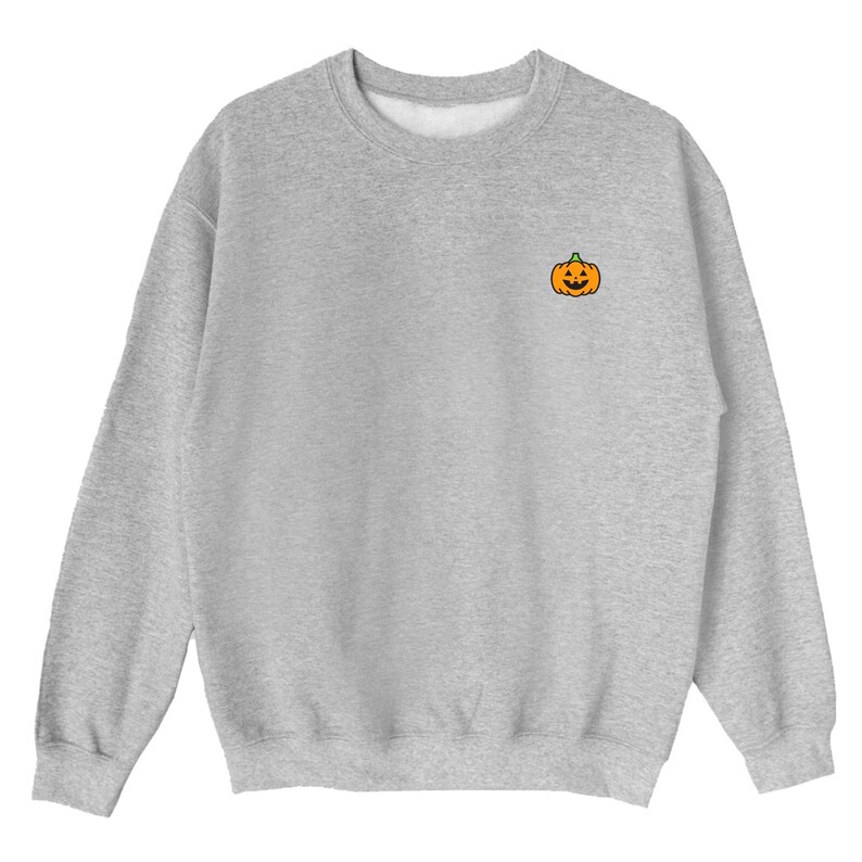 Puede incluir: Una sudadera gris con una peque&ntilde;a calabaza naranja con una cara de calabaza tallada bordada en el pecho izquierdo.