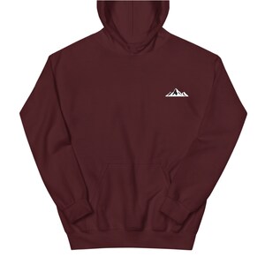 Op de afbeelding: Een bordeauxrode hoodie met een witte bergafbeelding op de linkerbovenborst. De hoodie heeft een capuchon met trekkoord en een kangoeroezak aan de voorkant. De stof ziet er zacht en comfortabel uit.