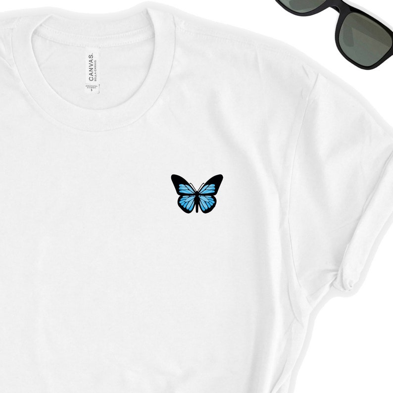 May include: White t-shirt with a blue butterfly graphic on the left chest.
