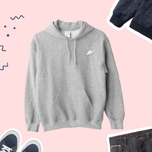 K&ouml;nnte beinhalten: Ein grauer Kapuzenpullover mit einem kleinen wei&szlig;en UFO-Motiv auf der Vorderseite. Der Pullover hat eine K&auml;ngurutasche und eine Kapuze mit Kordelzug.