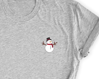May include: A light gray t-shirt featuring a small, embroidered snowman design. The snowman has a black top hat, a red scarf, and twig arms. The design is located on the left chest area of the shirt.