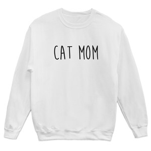 May include: White long-sleeved sweatshirt with the text "CAT MOM" printed in black on the front.