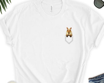 Könnte beinhalten: Weißes T-Shirt mit einer kleinen Tasche auf der Vorderseite. Ein Eichhörnchen schaut aus der Tasche.