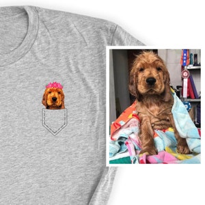 May include: Gray t-shirt featuring a pocket design with a Cocker Spaniel wearing a pink flower crown. The image on the right shows a wet Cocker Spaniel puppy wrapped in a towel. The shirt is a casual, everyday wear item.