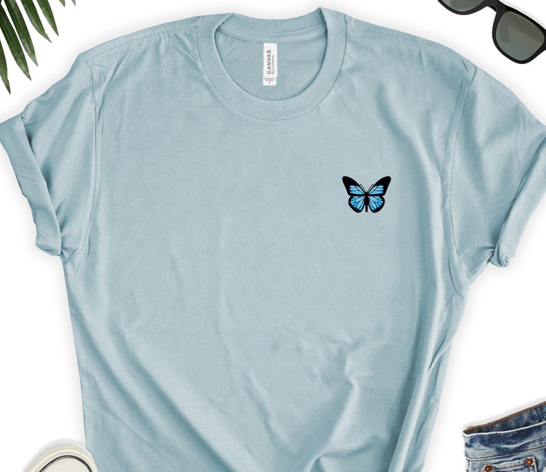 May include: A light blue t-shirt with a small blue butterfly graphic on the left chest.