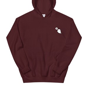 May include: A maroon hoodie with a front pocket and hood. A small white ghost graphic with the word "BOO" in a speech bubble is on the upper left chest area. The hoodie is made of a soft material.