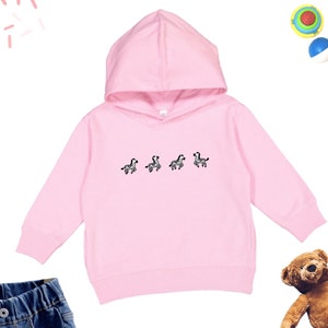 May include: A pink hooded sweatshirt with a graphic of four zebras on the front. The sweatshirt has long sleeves and a kangaroo pocket.