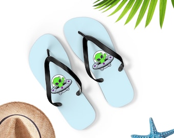May include: A pair of light blue flip flops with a black strap and a cartoon alien in a flying saucer graphic.