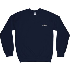 K&ouml;nnte beinhalten: Ein marineblauer Pullover mit einem kleinen gestickten Fischdesign auf der linken Brust.