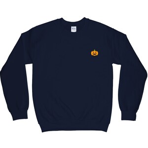 Puede incluir: Una sudadera azul marino con un peque&ntilde;o gr&aacute;fico de calabaza naranja en la parte delantera.