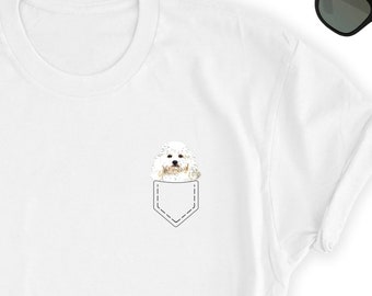 May include: White t-shirt with a small pocket on the front. A white dog with brown eyes is peeking out of the pocket.