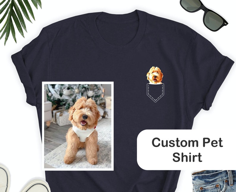 May include: Navy blue t-shirt with a custom pet design. The shirt features a pocket design with a dog's face and a framed photo of the dog. The text "Custom Pet Shirt" is displayed on the shirt. Sunglasses are placed on the top right.
