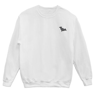 May include: White long-sleeved sweatshirt with a small black bat graphic on the left chest.