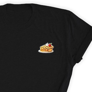 Puede incluir: Camiseta negra con una imagen de dibujos animados de una rebanada de pastel de manzana con una cereza y crema batida en la parte superior.