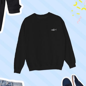 K&ouml;nnte beinhalten: Schwarzer Langarm-Pullover mit einem kleinen gestickten Fischdesign auf der linken Brust.