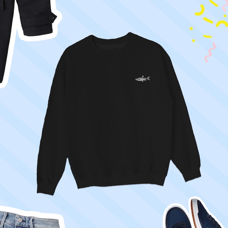 K&ouml;nnte beinhalten: Schwarzer Langarm-Pullover mit einem kleinen gestickten Fischdesign auf der linken Brust.