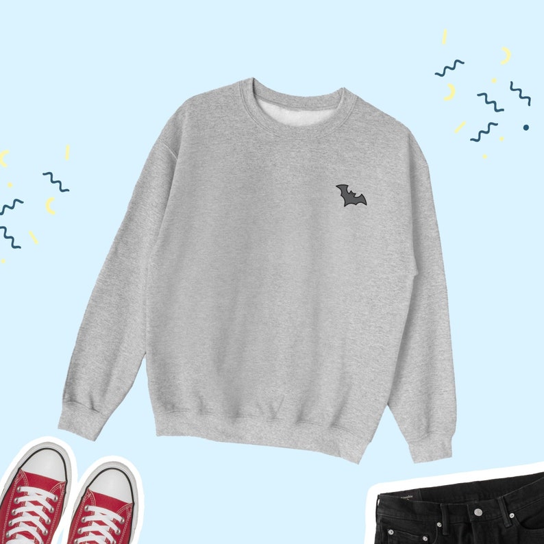 May include: A gray sweatshirt with a small black bat embroidered on the left chest. The sweatshirt is a classic crew neck style with long sleeves and a relaxed fit.
