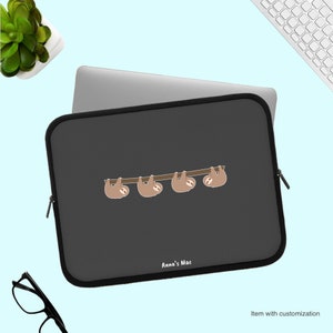 May include: A black laptop sleeve with a zipper closure. The sleeve has a graphic of four sloths hanging from a branch. The text "Anna's Mac" is printed on the sleeve.
